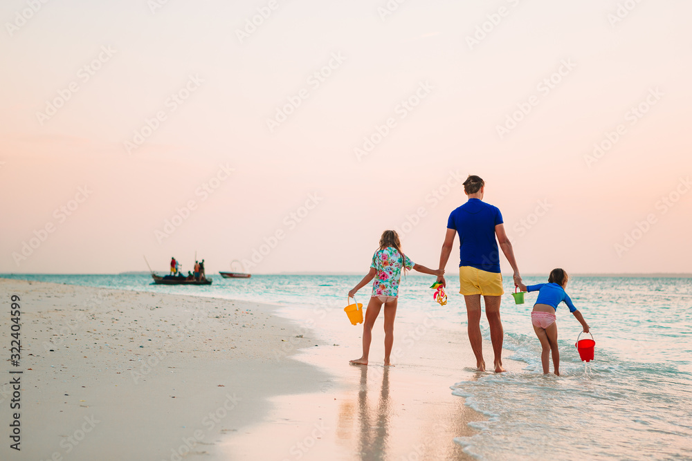 Happy father and his adorable little daughters at tropical beach having fun