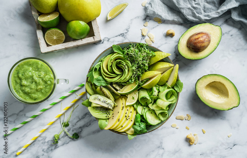 Fresh summer salad with avocado, kiwi, apple, cucumber, pear, micro greens, lime and sesame with smoothie on light marble background. Healthy food, clean eating, Buddha bowl salad, top view