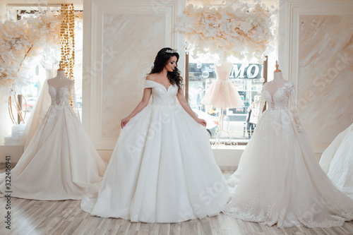 Young happy bride looking for beautiful wedding dress, future bride came in designers salon, lovely woman dream about wedding. Beautiful bride choosing wedding dress in a wedding salon