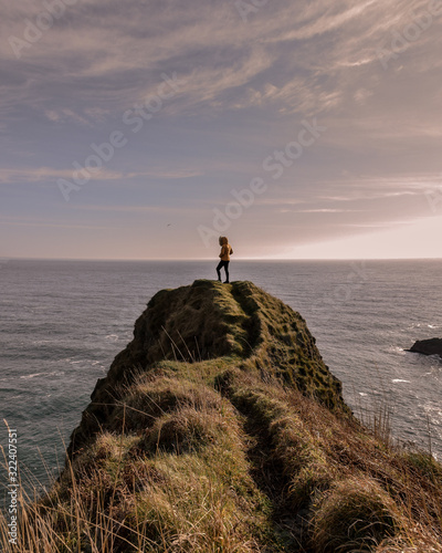 Girl in a cliff with a yellow jacket looking at the sea