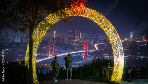 Male tourists on camlica hill are taking a photograph of the bridge and city scape of Istanbul with decorations around. Romantic colorful Turkey at night. photo