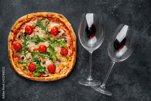 Delicious Italian pizza with mozzarella cheese, mushrooms, tomato, bell pepper and onion. glasses of wine on a stone background