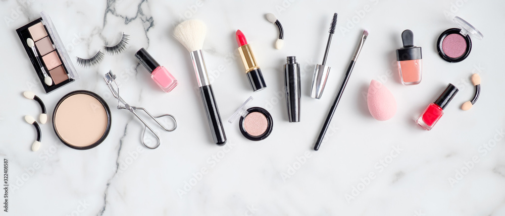 Makeup cosmetic products and accessories spilling out on to marble background. Flat lay, top view