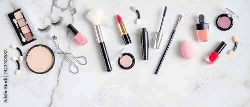 Makeup cosmetic products and accessories spilling out on to marble background. Flat lay, top view