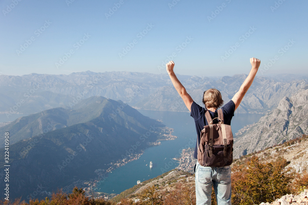 Obraz premium Traveler with backpack on mountain top. Happy man with raised hands at background of amazing landscape. Tourist enjoying traveling, adventure, freedom, victory. Copy space. Rear view.