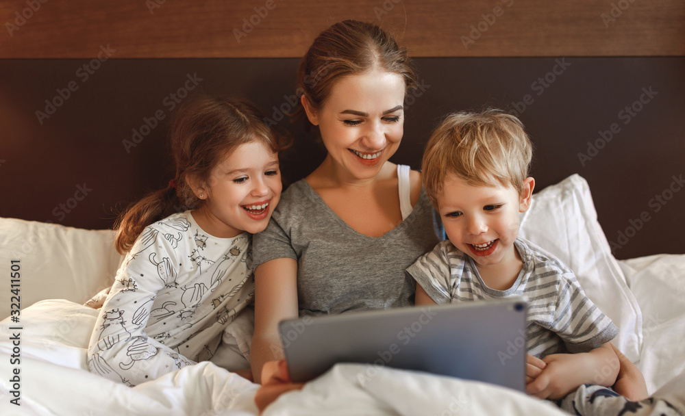 happy family mother and children with tablet computer at home in bed in evening. happy family mother and children with tablet computer at home in bed in evening.