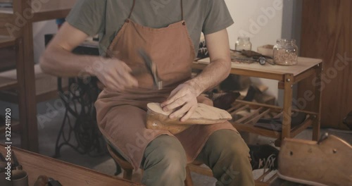 Traditional bespoke shoemaker nailing leather insole on wooden shoe last in workshop
