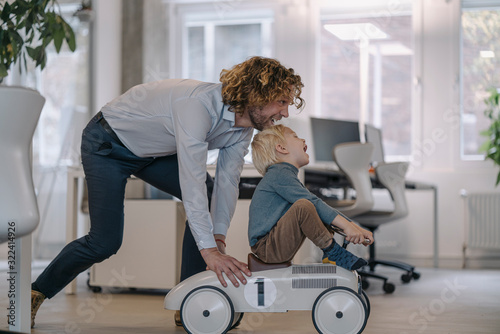 Businessman pushing son on toy car in office photo