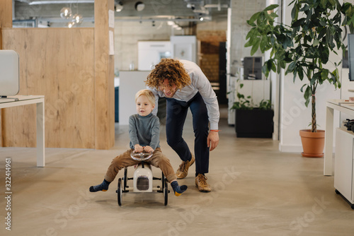 Businessman pushing son on toy car in office photo