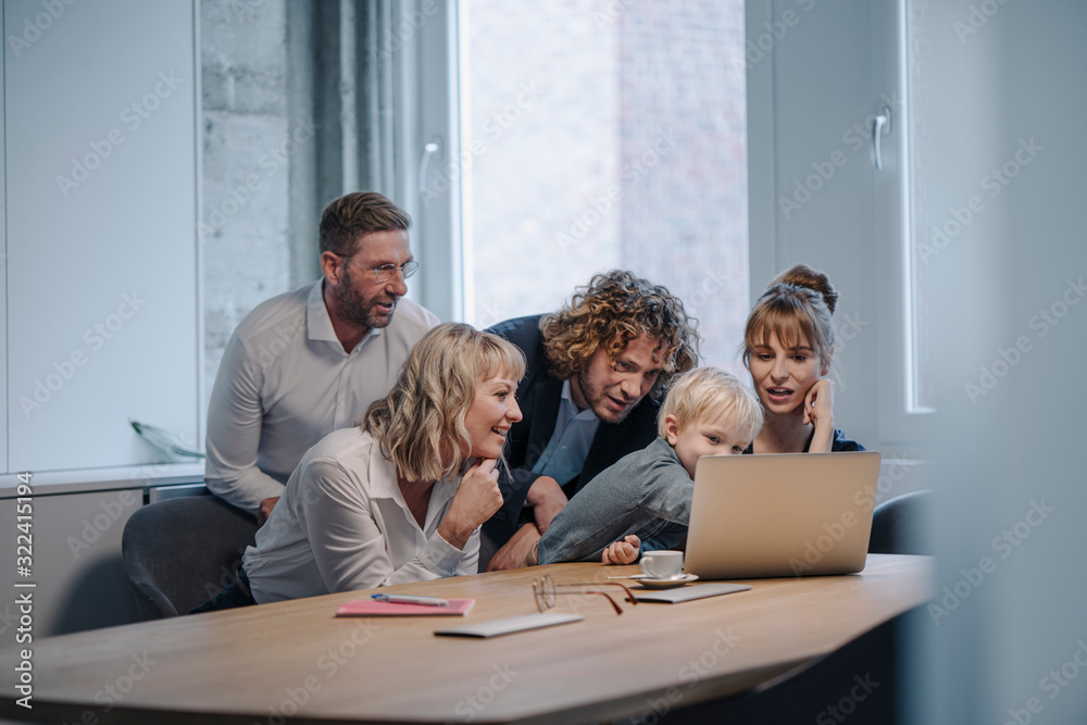 Business team with boy looking at laptop in office Business team with boy looking at laptop in office