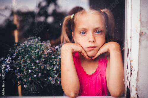 Little cute girl with blond hair and pink dress with beautiful flowers behind the window © benevolente