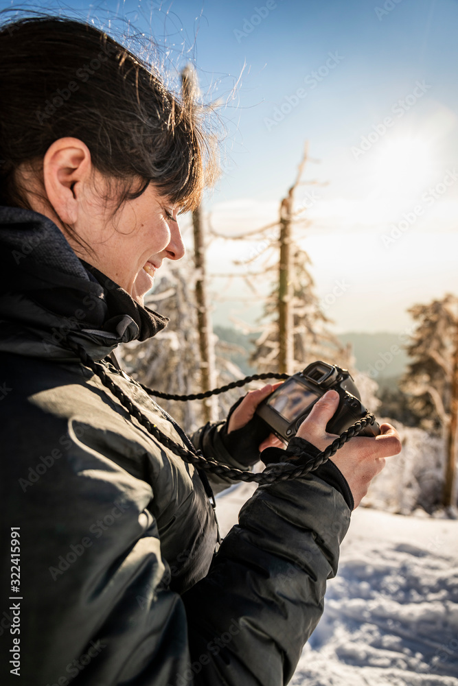 Smiling woman checking display of camera in winter at Hornisgrinde, Black Forest, Germany Smiling woman checking display of camera in winter at Hornisgrinde, Black Forest, Germany