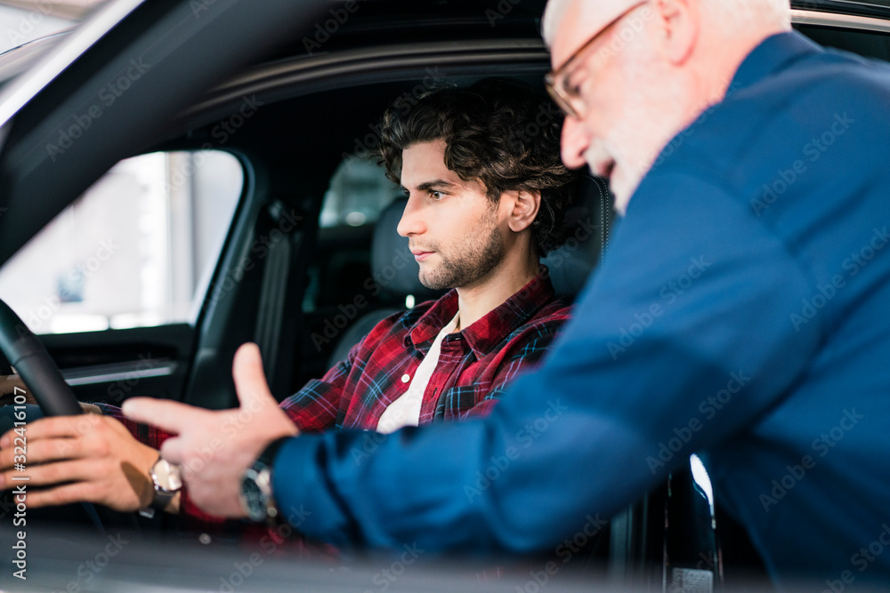 Car dealer showing car to young man in showroom Car dealer showing car to young man in showroom
