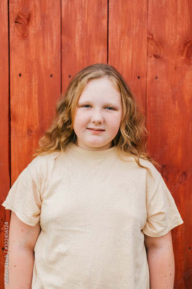 Beautiful chubby girl with long hair in yellow t-shirt stands against the wooden wall in village Beautiful chubby girl with long hair in yellow t-shirt stands against the wooden wall in village