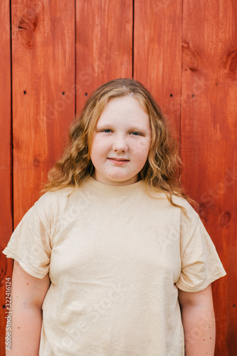 Beautiful chubby girl with long hair in yellow t-shirt stands against the wooden wall in village © benevolente