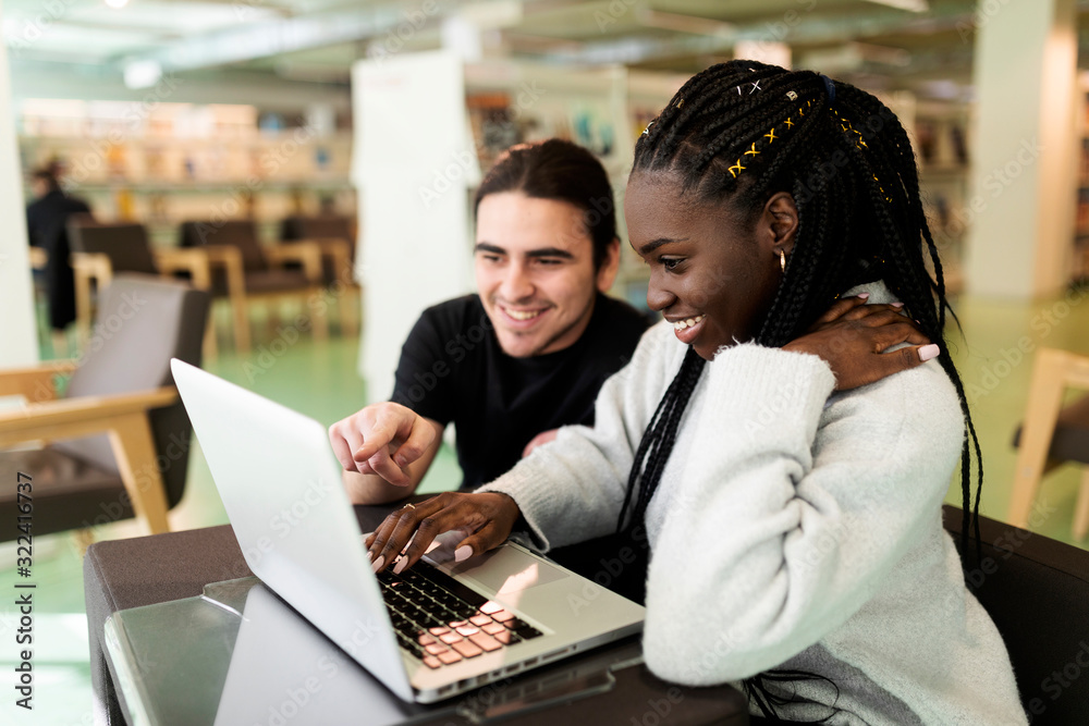 Two smiling students using laptop in a library Two smiling students using laptop in a library