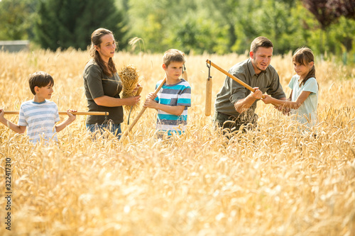 Children learning how to flail wheat in field