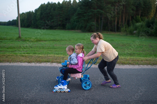 Funny young girl in pink hoody roller-skates on a trolley in the evening with her sisters