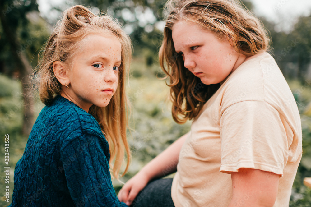 Fototapeta premium Portrait of young lovely girl with her elder chubby sister lie on the coverlet in the garden and smile