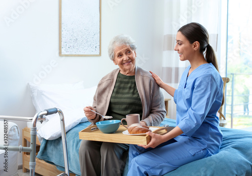 Care worker serving dinner for elderly woman in geriatric hospice