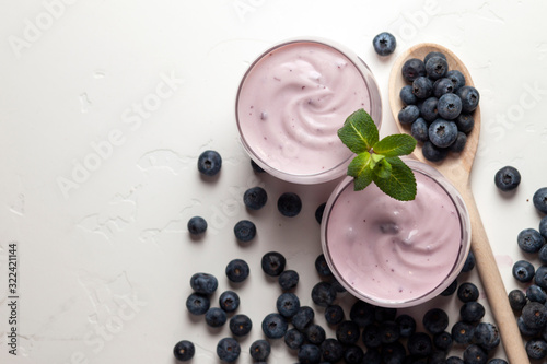 two glasses of blueberry yogurt on a white table with berries, homemade fresh milkshake with wild berries