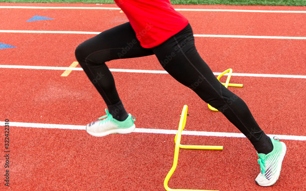 Obraz premium Sprinter performing running drill over yellow mini hurdle on a track