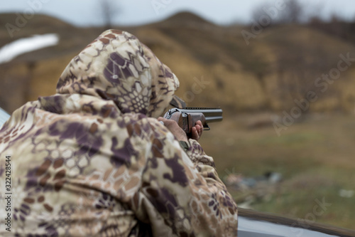 A hunter in camouflage at the shooting range calibrates the weapon. A man shoots at targets.
