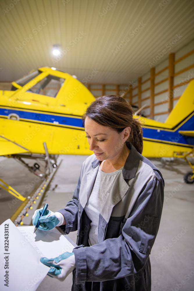Female pilot with clipboard examining crop sprayer inside airplane