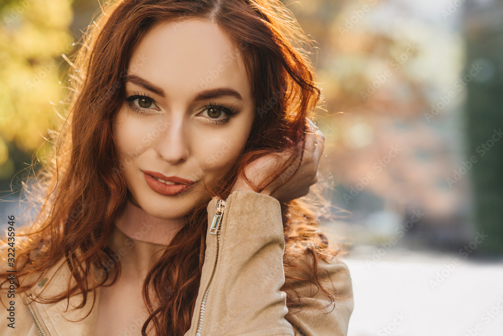 Fototapeta premium Close-up portrait of sensual young woman playing with dark ginger hair. Dreamy red-haired girl posing with smile on blur background.