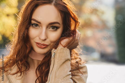 Close-up portrait of sensual young woman playing with dark ginger hair. Dreamy red-haired girl posing with smile on blur background.