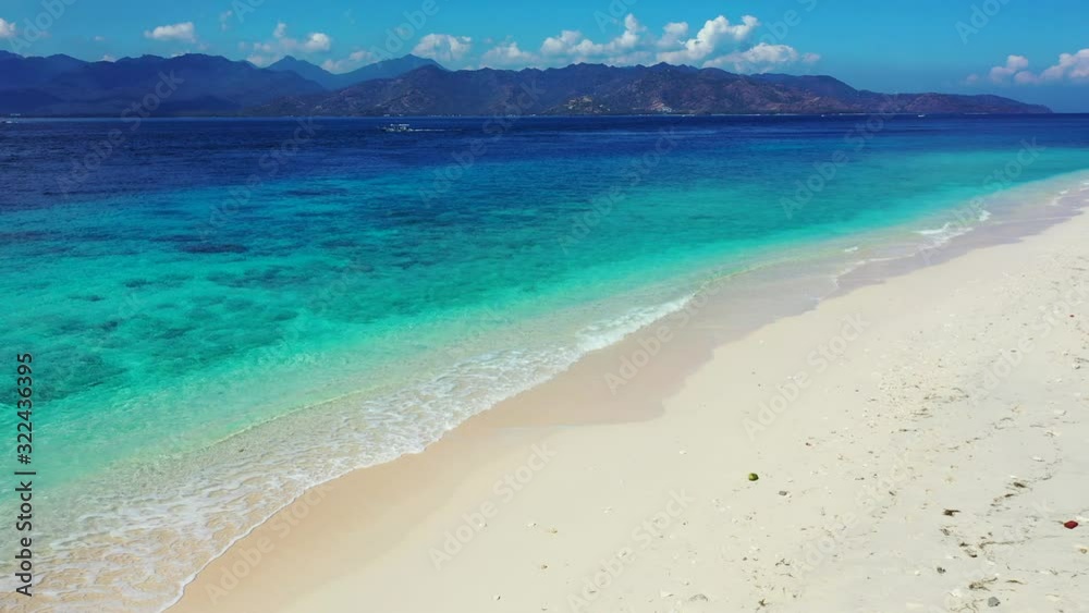 Calm clear water of blue turquoise sea with white waves washing sandy beach of tropical island, bright sky over mountains in Indonesia Calm clear water of blue turquoise sea with white waves washing sandy beach of tropical island, bright sky over mountains in Indonesia