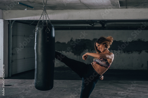 Young sportswoman doing high kick during boxing exercise in a garage.