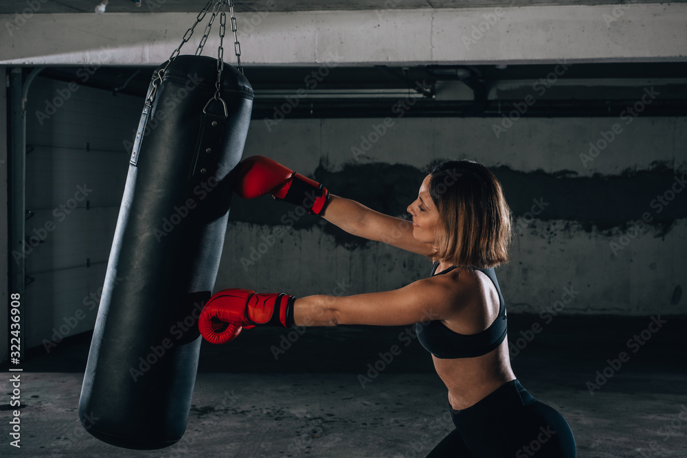 Profile view of a strong young woman punching a boxing bag inside the garage