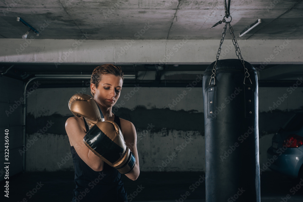 Strong woman with short hair putting on her gold boxing gloves