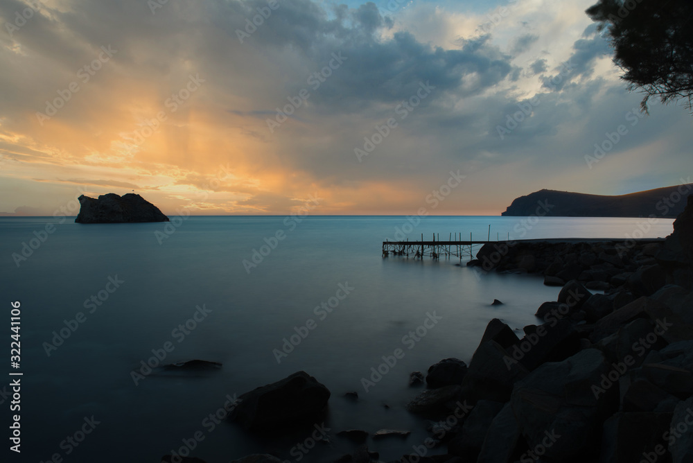 Fototapeta premium dilapidated, rundown pier with island in the background at sunset