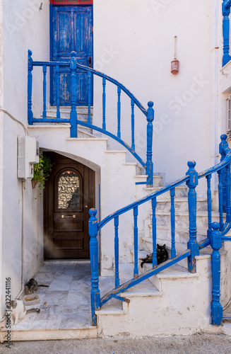 3 cats laying down on stairs with blue railing in front of a traditional Greek house