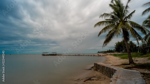 Palm tree and walkeway in front of Dilapidated old fishing dock collapsing into the sea in Pak Nam Pran Thailand