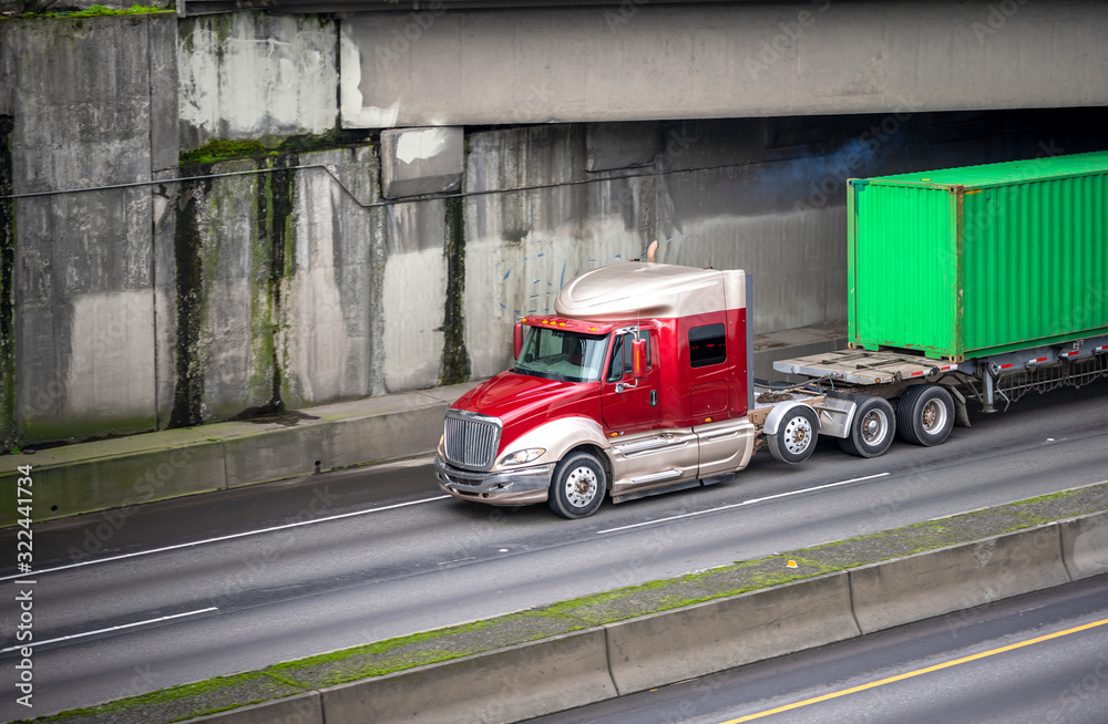 Fototapeta premium Big rig low cab semi truck transporting green container on flat bed semi trailer running on the road overpass intersection and bridge