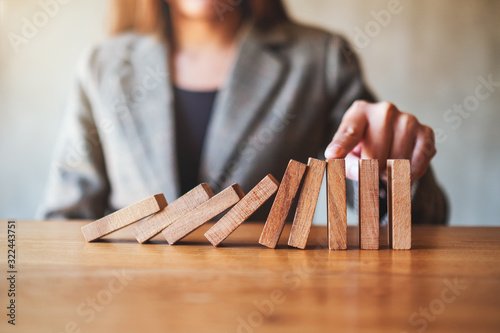 Closeup image of a businesswoman's finger try to stopping falling wooden dominoes blocks for business solution concept