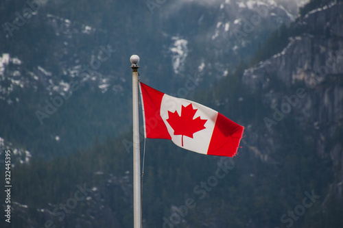 A picture of Canada flag waving against the mountain lightly dusted with snow. Squamish BC Canada