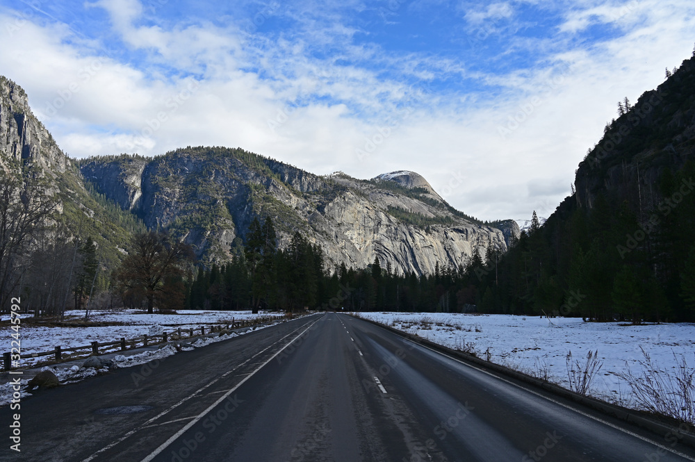 Road in Yosemite Valley in Yosemite National Park, California with granite rock formations in background under winter cloudscape.