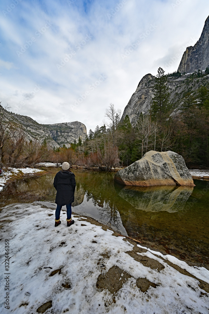 Young woman enjoying view of granite rock formations reflected in Mirror Lake in Yosemite National Park, California.
