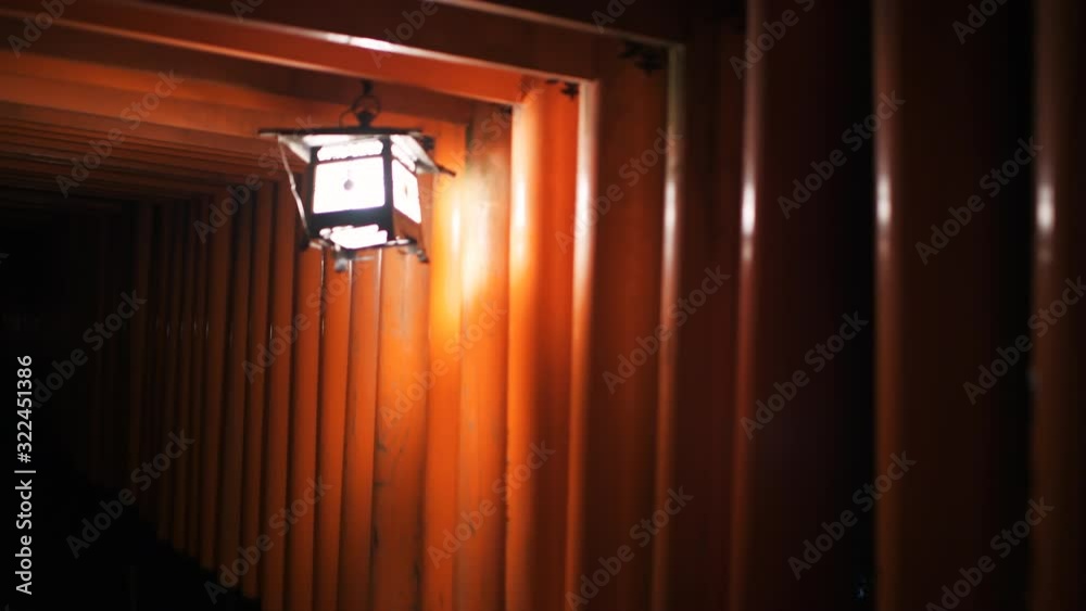 Kyoto, Japan panning orange red vermilion Fushimi Inari shrine torii gates in park at night with illumination lantern light or lamp with kanji Japanese text