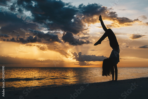 Tablou pe pânză A woman doing a graceful handstand on the beach in silhouette