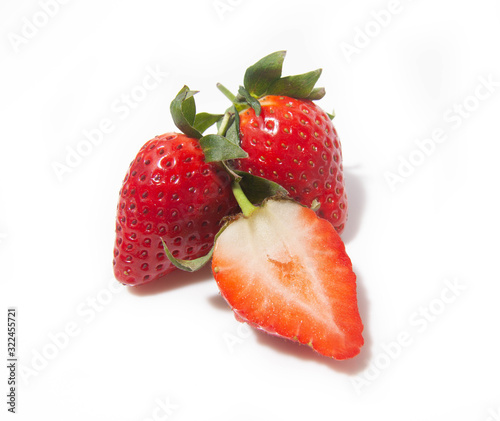 three strawberries, one half and two whole ones behind it, are isolated on a white background