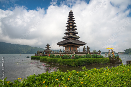 The scenery of the Pura Ulun Danu temple at Beratan lake in cloudy day with green grass and yellow flowers foreground at Bali, Indonesia.