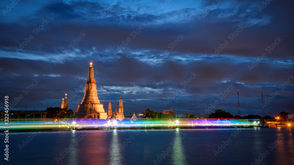 The scenery of Wat Arun (temple of dawn) with a blue sky after sunset time with the colorful light from the boat that pass through Chaopraya river in Bangkok, Thailand.