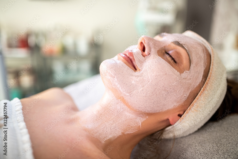 Naklejka premium A young woman lying on a bed with a beauty face mask at the dermatologist.