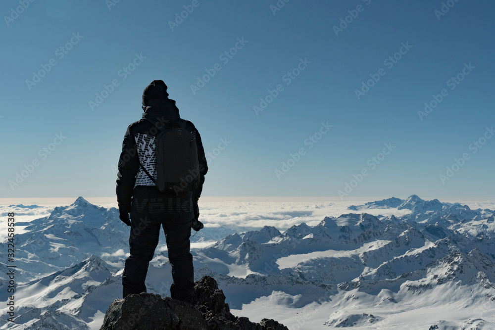 Male adult photographer standing on top of the mountain. Caucasus mountains landscape.  Male backpacker in winter clothing. Sunny day at the mountains. Hiking concept.