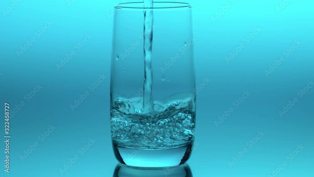 Close up clear drinking simple water pouring into transparent glass in slow motion on blue background. Healthy lifestyle concept. Simplicity Close up clear drinking simple water pouring into transparent glass in slow motion on blue background. Healthy lifestyle concept. Simplicity